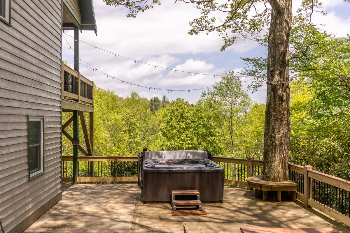 This image captures the outdoor hot tub nestled on the deck, surrounded by lush trees and enhanced by welcoming string lights. The setting exudes a peaceful, social vibe that's perfect for evening relaxation or celebrations after a day of adventure.