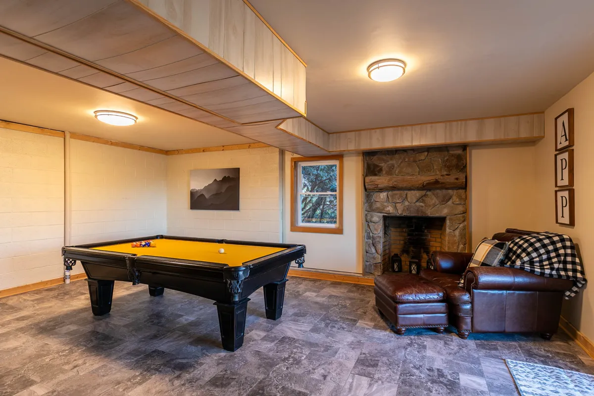 A relaxed and casual space featuring a pool table, leather armchair, fireplace, and framed artwork. The room radiates warmth and camaraderie, suggesting a spot equally suited for games, relaxation, and conversation.