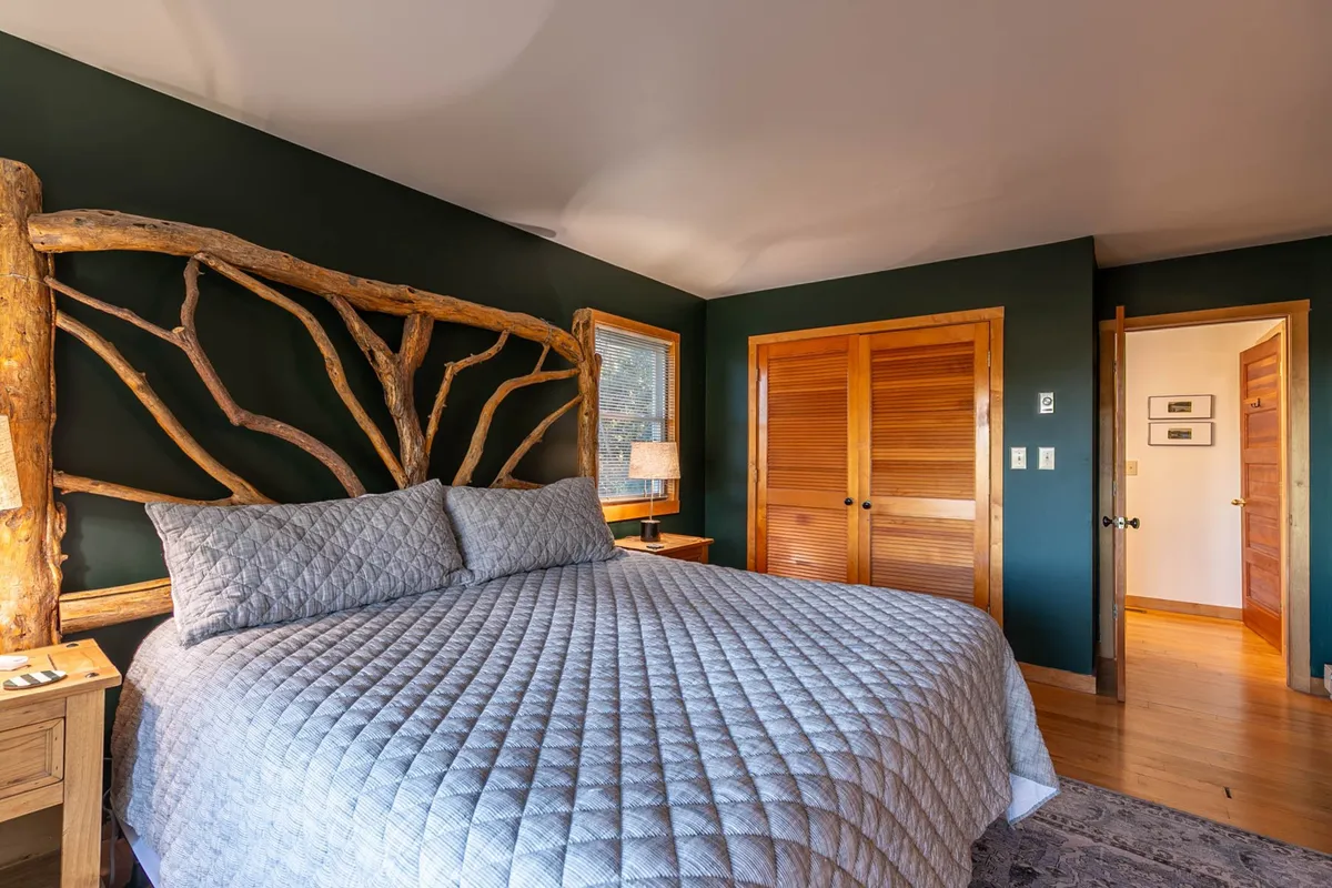 A tranquil bedroom scene with a rustic wooden headboard, plush bedding, and soft morning light filtering in. The setting feels private and calming, evoking the idea of starting the day peacefully in seclusion.