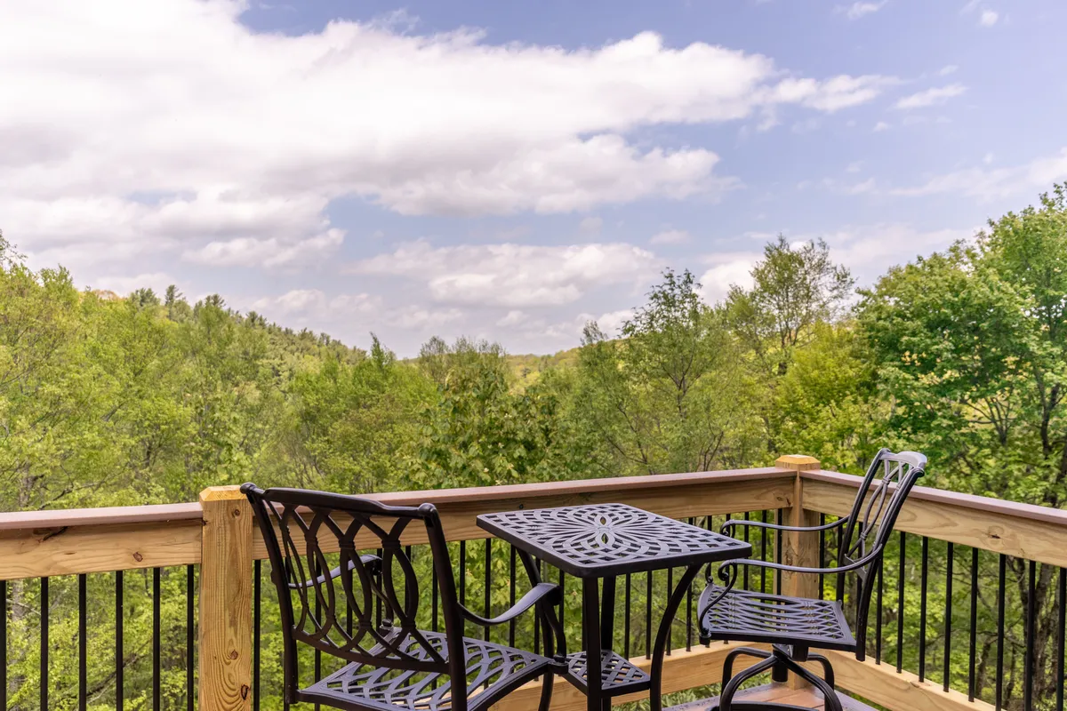 A wooden deck with metal patio furniture overlooks an expansive view of trees, setting the scene for outdoor gatherings, morning coffee, or evening stargazing. The relaxed ambiance invites guests to share stories and enjoy the exclusivity of the location.
