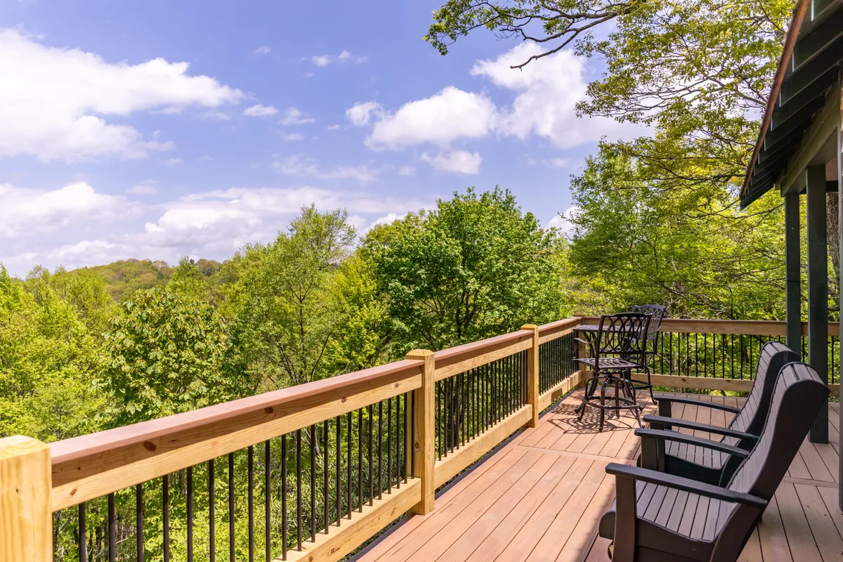 A peaceful wooden deck with comfortable chairs, nestled among tall green trees and open sky. The setting creates a perfect nook for sipping coffee, reading, or simply enjoying the fresh mountain air and sounds of wildlife.