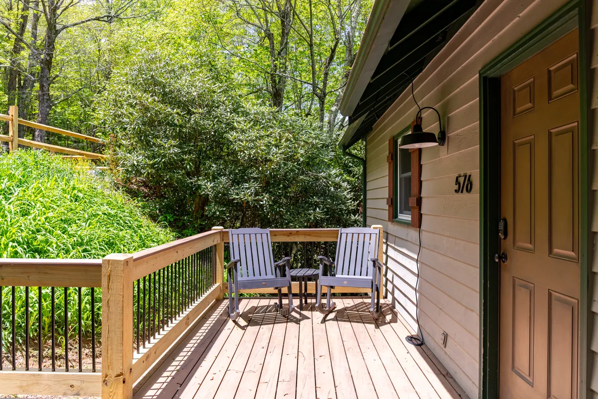 A tranquil view of a wooden deck with two chairs and a small table, surrounded by lush greenery. The setting is peaceful and ideal for enjoying mountain vistas and quiet moments outdoors with your pet.