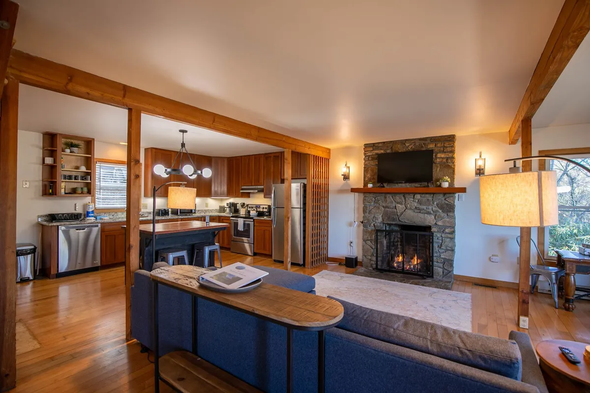 A view of the open kitchen with granite counters and a central island, adjacent to a fireplace and large window. The kitchen area feels modern yet inviting, with space for cooking together or enjoying a cup of coffee at the island.