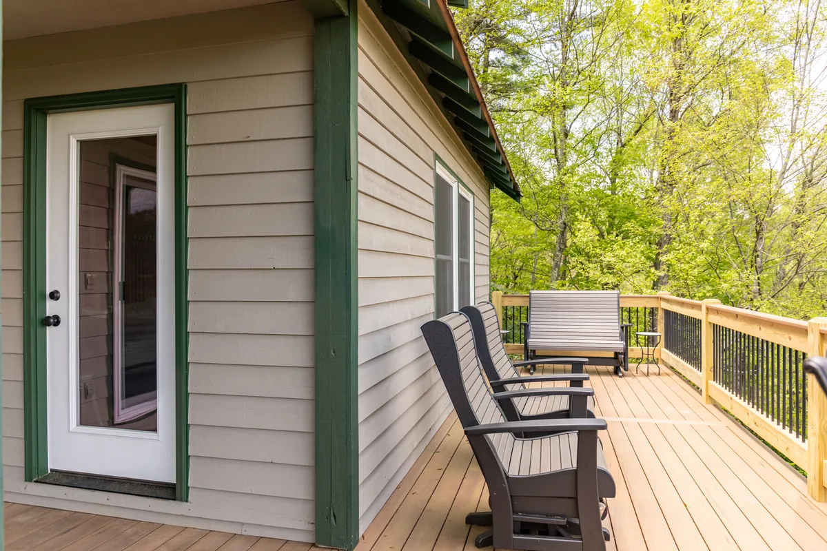 Deck chairs sit on a rustic wooden deck bathed in morning light, with green foliage all around and the entrance door visible. The scene invites families to relax, enjoy coffee, and reflect on their adventures together.